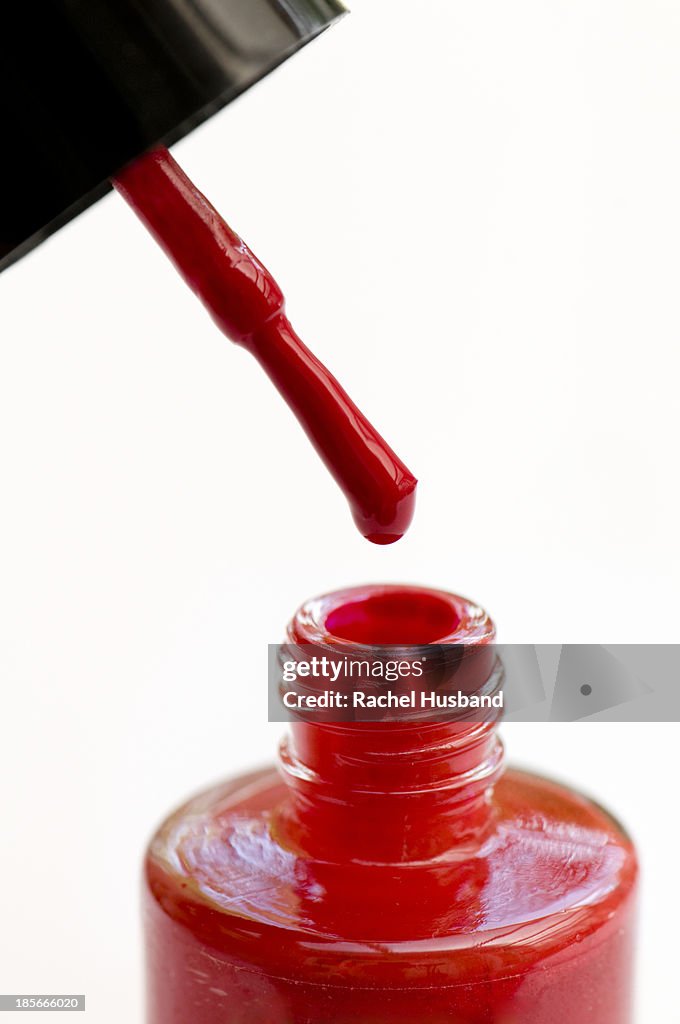 Red nail varnish dripping off brush into pot