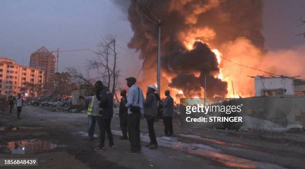 This image grab taken from AFPTV video footage on December 18, 2023 shows people in front of the flames from the fire at Conakry's main fuel depot....