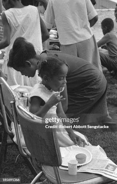 View of children eating a picnic lunch while seated on grass along the Bud Billiken parade route, Chicago, Illinois, mid to late 1960s .