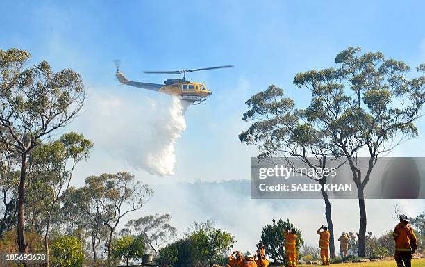 Firefighters watch a helicopter drop water to douse fires approaching houses in Faulconbridge in the Blue Mountains on October 24, 2013. Thousands of...