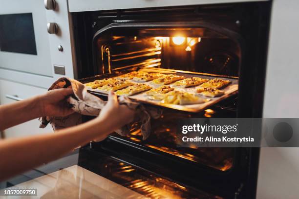 woman putting baking sheet with raw cookies into oven - backblech stock-fotos und bilder