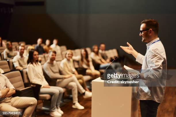 happy public speaker giving a speech in front of crowd in convention center. - conference speaker stock pictures, royalty-free photos & images