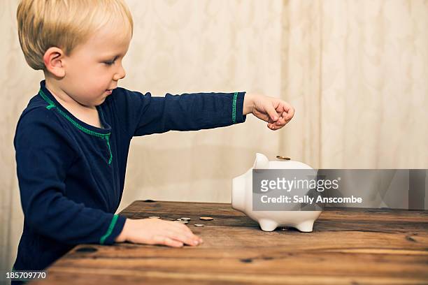 little boy saving his money in a piggy bank - positionner photos et images de collection