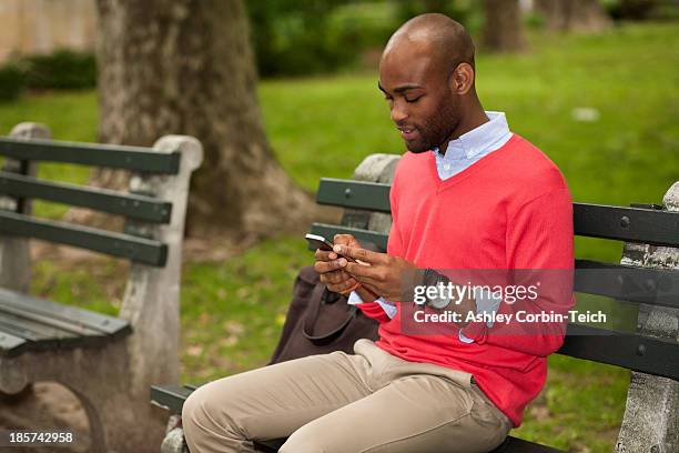 young man sitting on park bench using mobile phone - un solo hombre joven fotografías e imágenes de stock