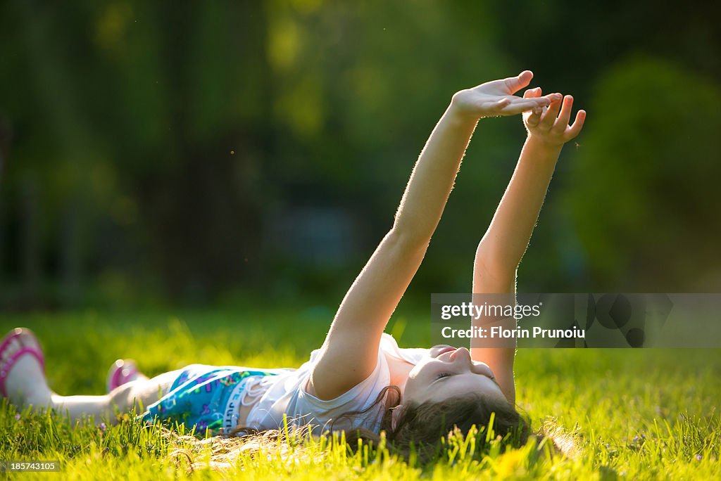 Girl lying on grass with arms raised