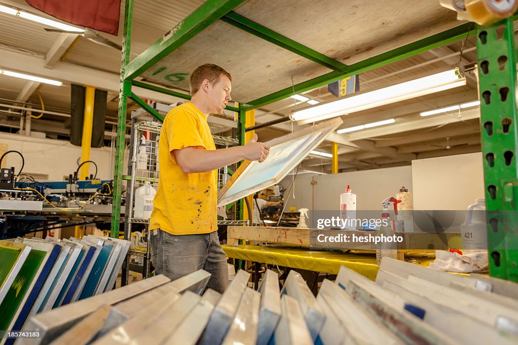 Worker carrying frame in screen printing workshop