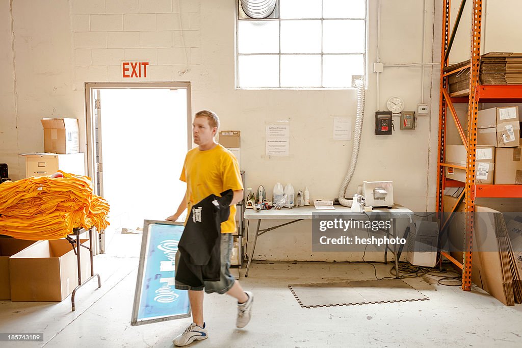 Worker carrying frame and t-shirt in screen printing workshop