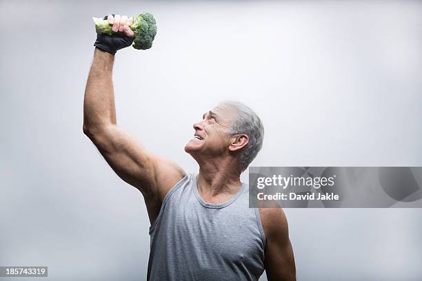 senior man looking up and lifting broccoli - funny vegetable stock pictures, royalty-free photos & images