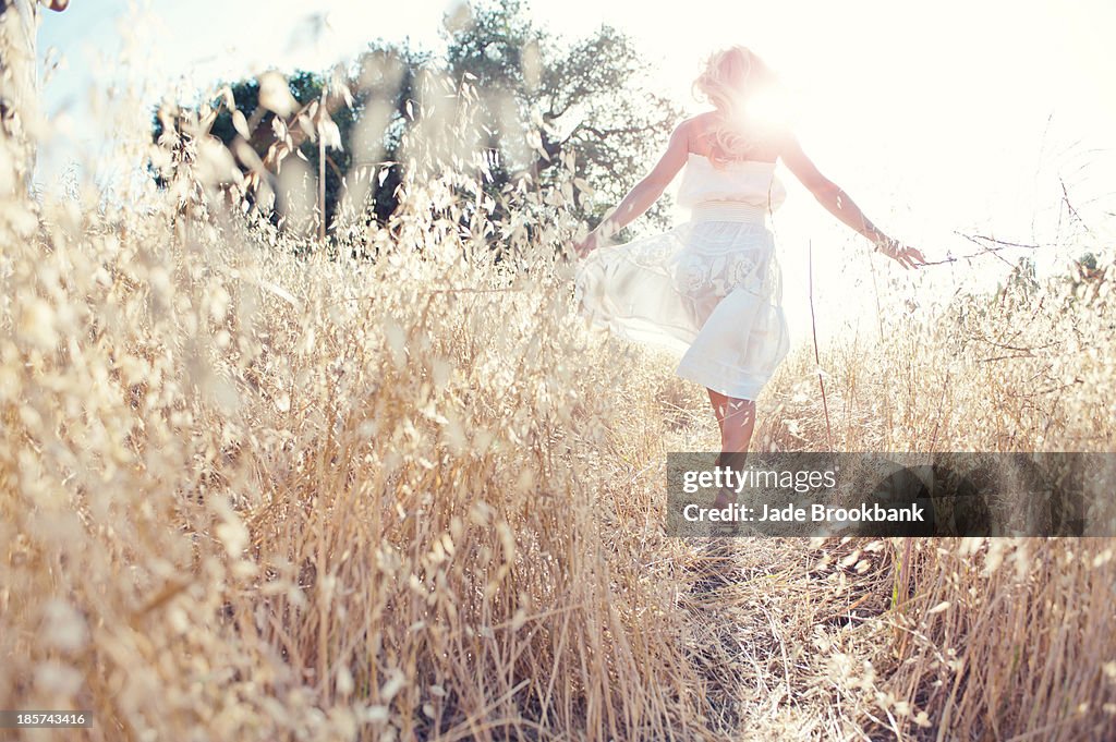 Woman walking through field touching grasses