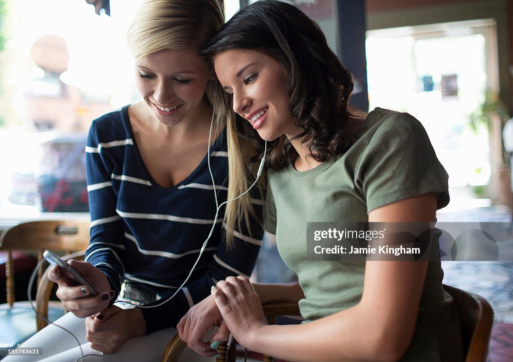 Two teenage girls sharing earphones in coffee house