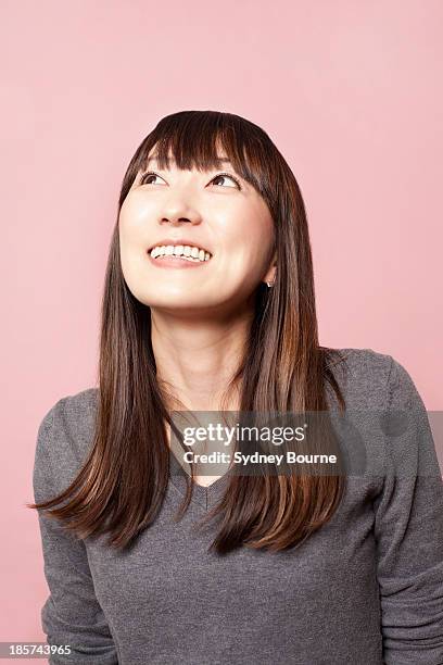 mid adult woman smiling and looking up against pink background - 女性　日本人　笑顔　30代 ストックフォトと画像