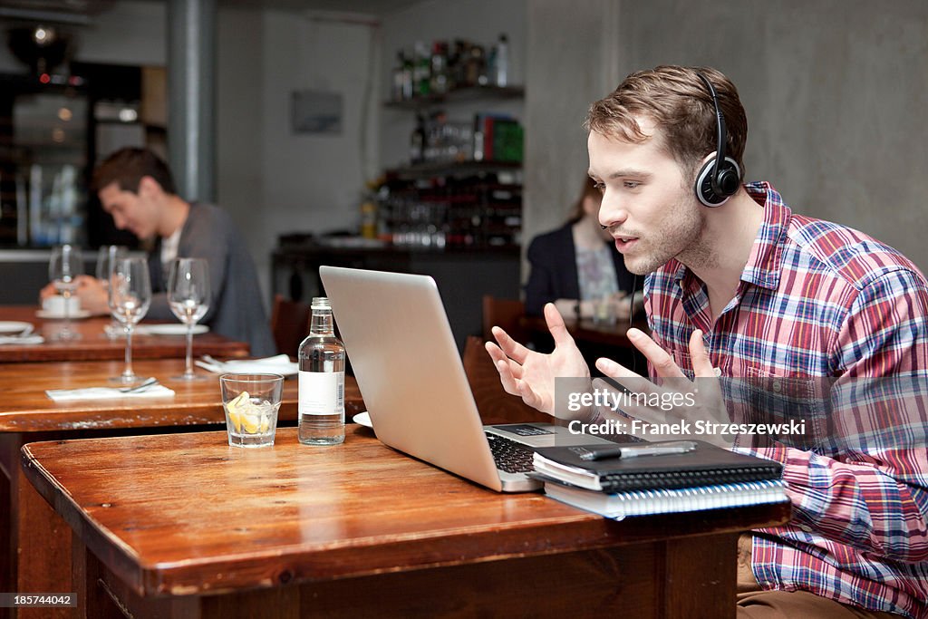 Young man wearing headphones using laptop in cafe