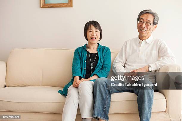 senior couple sitting on sofa,  portrait - japanese senior couple stockfoto's en -beelden