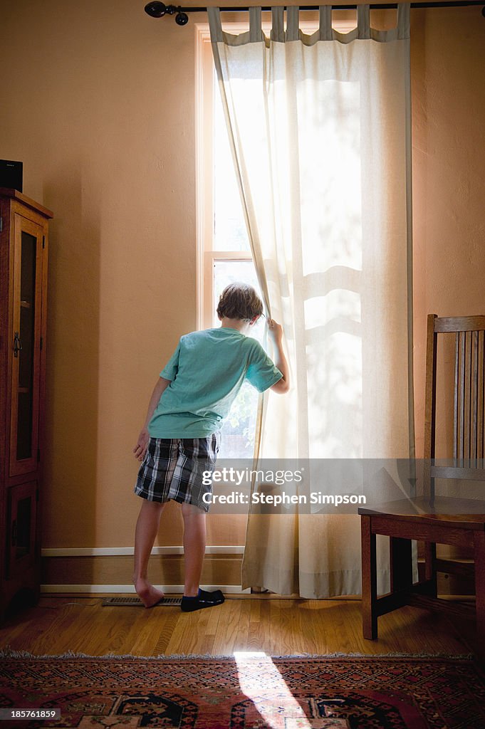 Boy looking out window, pulling curtain aside