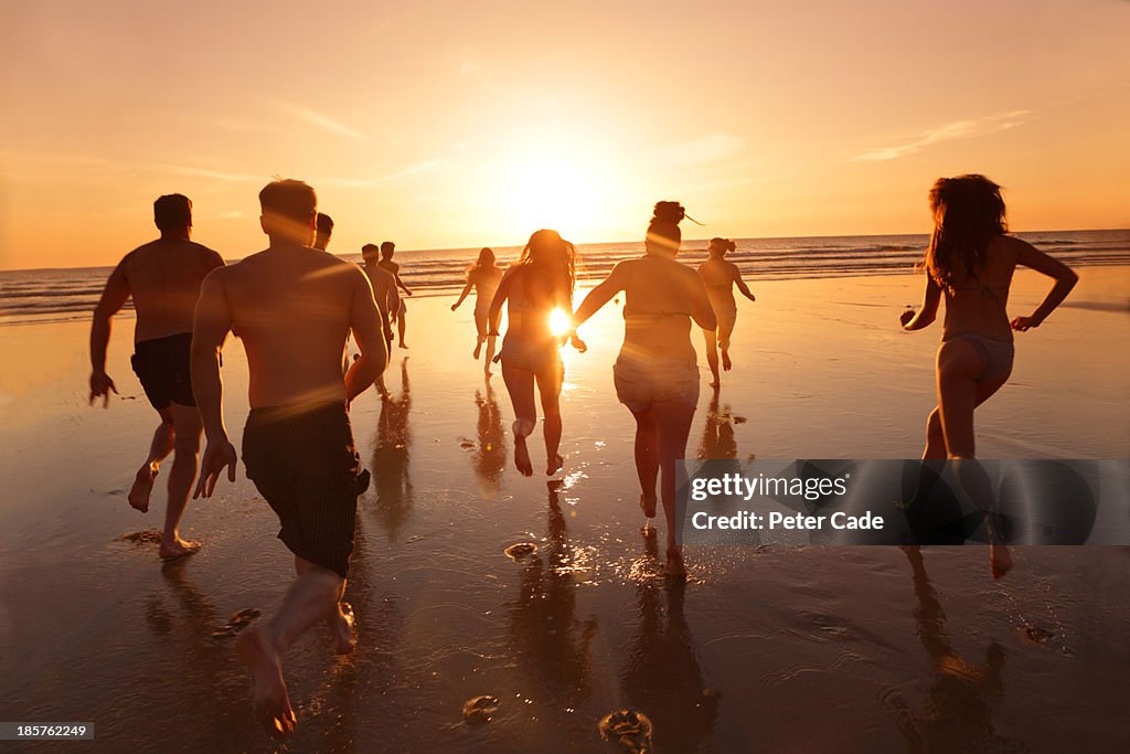 Group of young adults running into sea at sunset