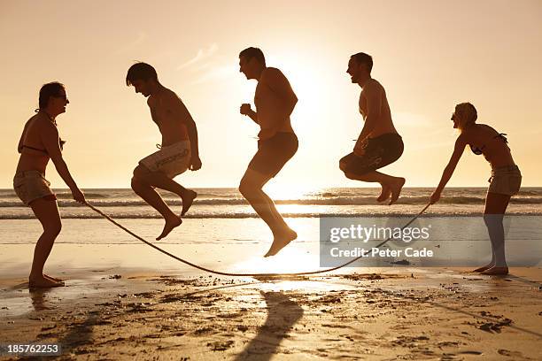 three men jumping over skipping rope on beach - friendly match stockfoto's en -beelden