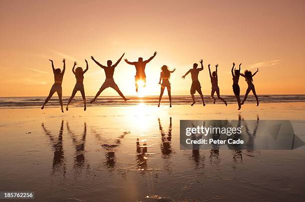 group of young adults jumping on beach at sunset - friends sunset imagens e fotografias de stock