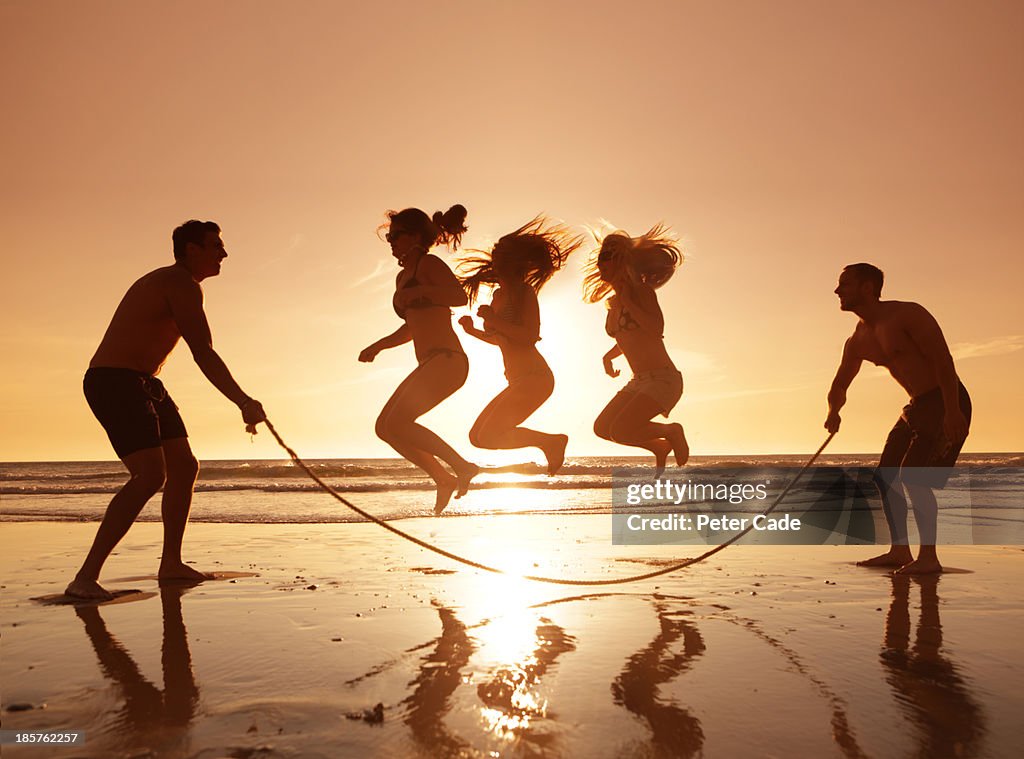 Three girls jumping over skipping rope on beach