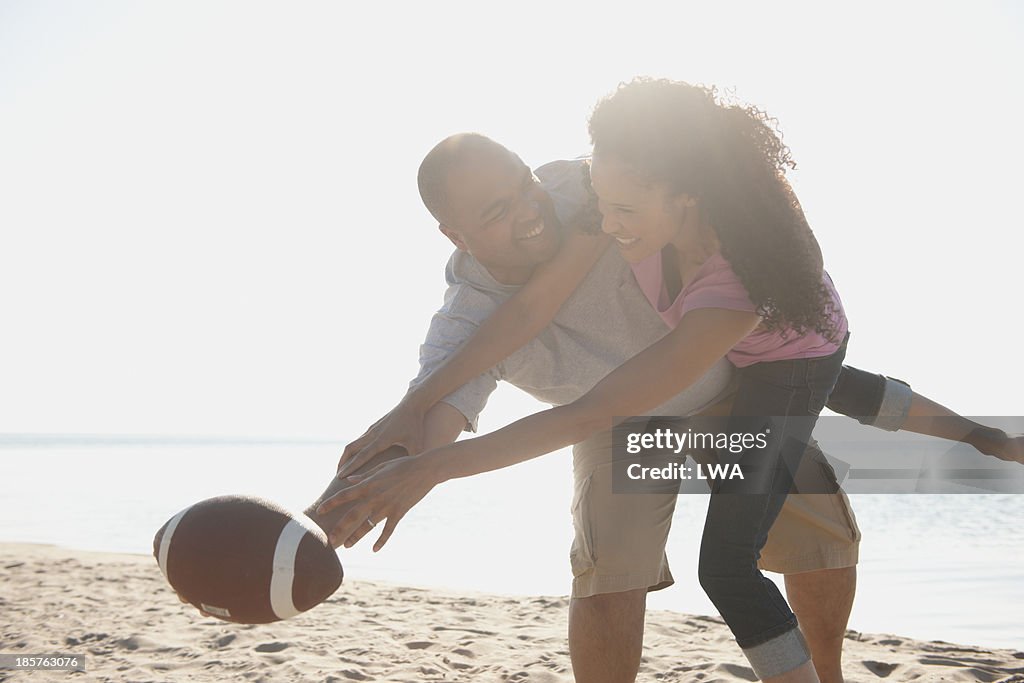 Black couple playing football on beach