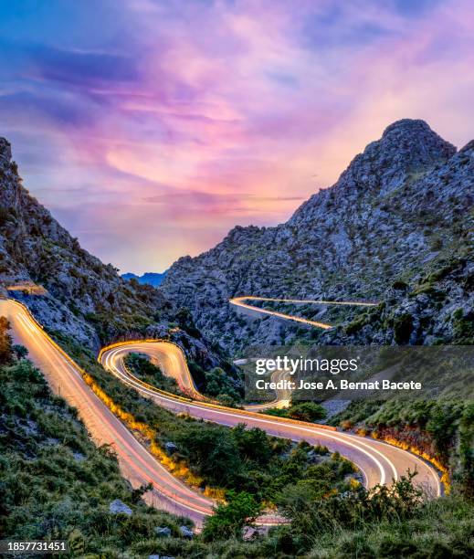 sunset on a curvy mountain road between ravines, with light trails from moving cars. - bernat bacete stock pictures, royalty-free photos & images