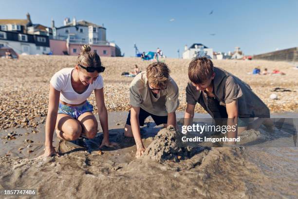 crianças adolescentes brincando na areia na praia de lyme regis durante a maré baixa - características do litoral - fotografias e filmes do acervo