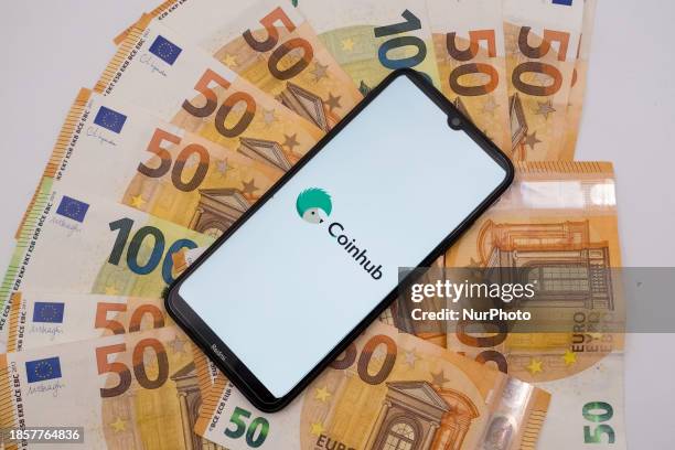 The Coinhub logo is being displayed on a smartphone screen that is placed on 50 and 100 Euro bills in Athens, Greece, on December 18, 2023.