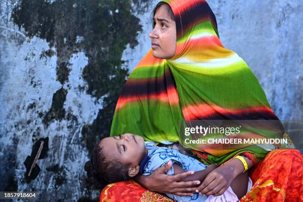 Rohingya refugee woman looks on as she holds her child at a temporary camp, at a port in Sabang island, Indonesia's Aceh province on December 18,...