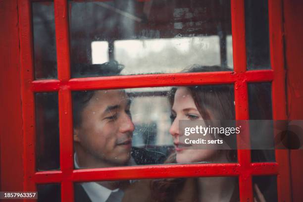 young romantic couple embarking on a blissful journey in london's iconic red telephone booth - confidential englischer begriff stock-fotos und bilder