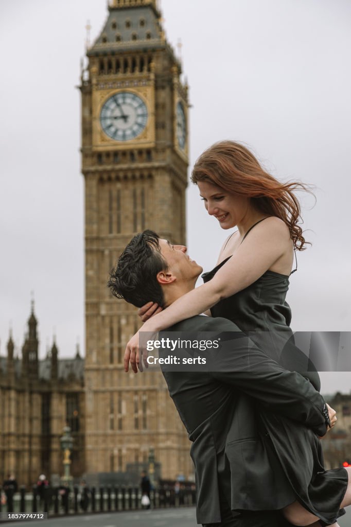 Portrait of a Happy Beautiful Couple Hugging and Spinning by Big Ben in London. Man lifting Woman in the Air