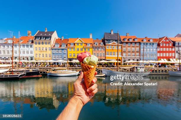 eating multi-colored ice cream with colourful vibrant houses of nyhavn harbour in background, copenhagen, denmark - wonderlust stockfoto's en -beelden