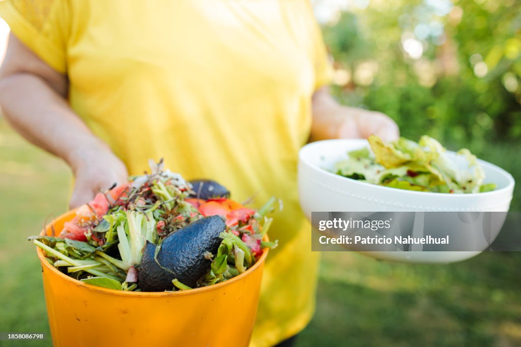 Senior Woman Carrying a Plastic Container Filled with Organic Waste, Ready to Be Deposited into the Compost for Eco-Friendly Recycling