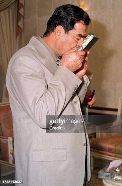 Iraqi President Saddam Hussein kisses a Koran he received as a gift 12 November 2000 in Baghdad from Palestinians injured during clashes with Israeli...