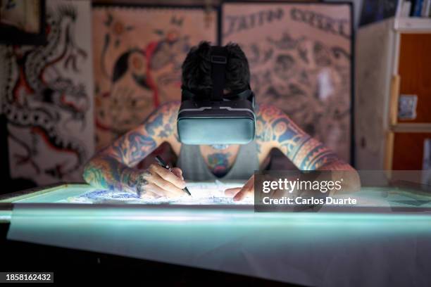 un tatuador en el diseño de estudio utiliza gafas de realidad virtual para dibujar un tatuaje y ver los colores cómo se verán - body art painting fotografías e imágenes de stock