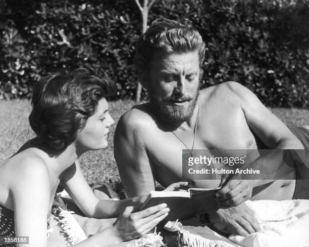 American actor Kirk Douglas looks at a book with his second wife, Anne Buydens, c. 1956.