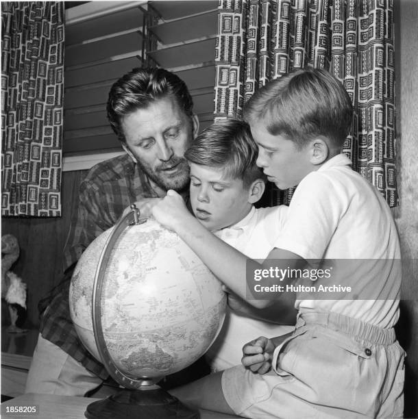 American actor Kirk Douglas looks at a world globe with two of his sons, Joel and Michael Douglas c. 1956.