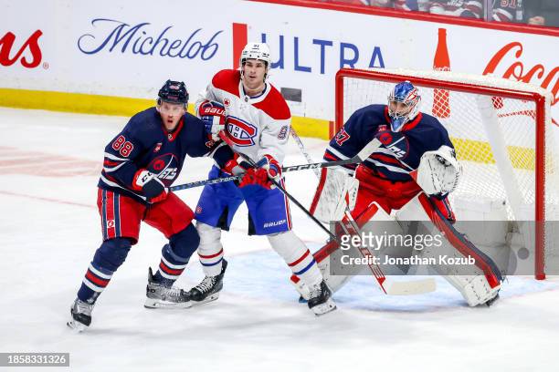 Sean Monahan of the Montreal Canadiens battles Nate Schmidt and goaltender Connor Hellebuyck of the Winnipeg Jets as they keep an eye on the play...