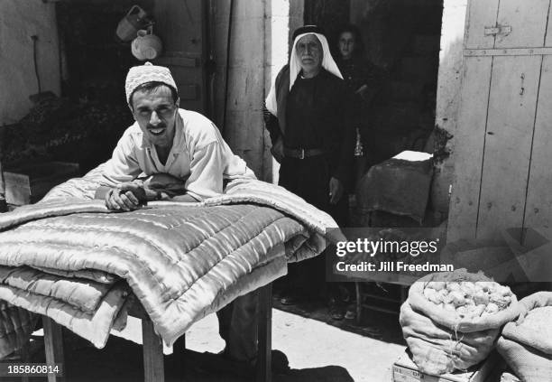 Market vendor sells fabric and vegetables in Hebron, West Bank, 1967.