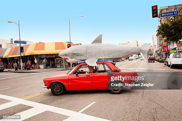 man driving car with papier-mache shark on roof - humor stockfoto's en -beelden