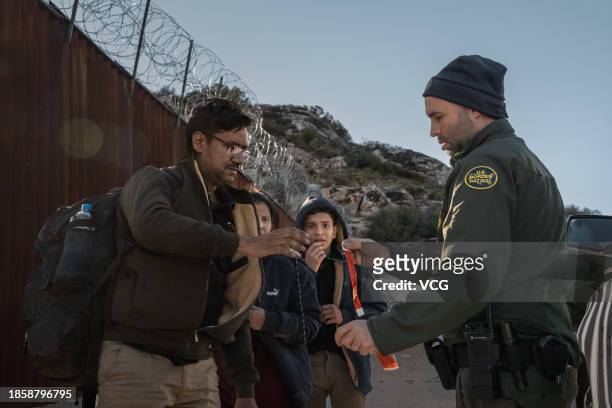 Asylum seeking migrants receive bracelets with their date of arrival from a U.S. Border Patrol agent after crossing from Mexico at a makeshift camp...