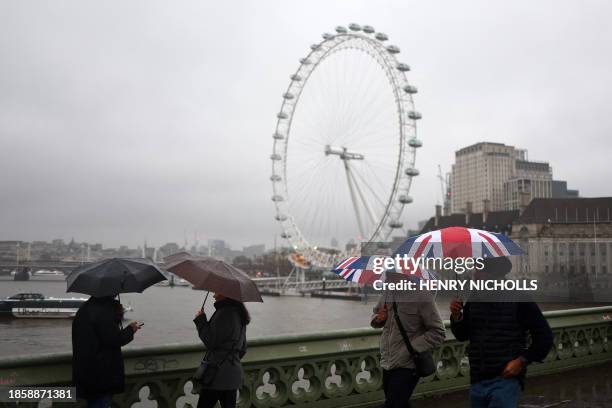 Pedestrians holding Union Jack umbrellas walk in the rain past the London Eye in central London on December 19, 2023.