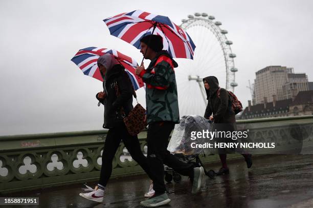 Pedestrians holding Union Jack umbrellas walk in the rain past the London Eye in central London on December 19, 2023.
