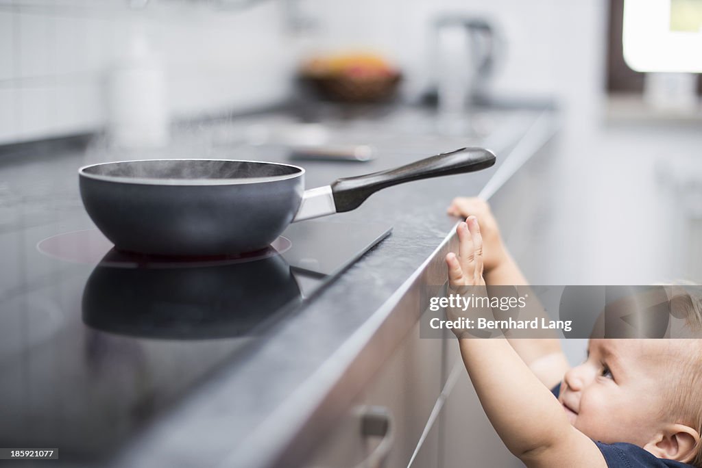 Little boy (1 y) trying to reach pan on stove
