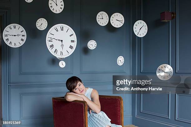 woman in armchair with hanging clocks above - frau uhr stock-fotos und bilder