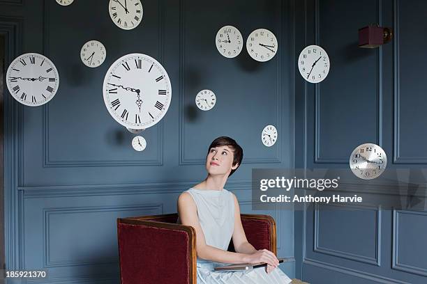 woman in armchair with hanging clocks above - multi colored dress photos et images de collection