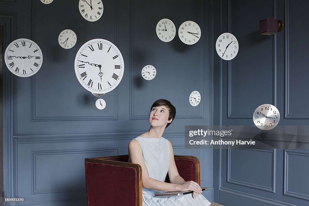 Woman in armchair with hanging clocks above
