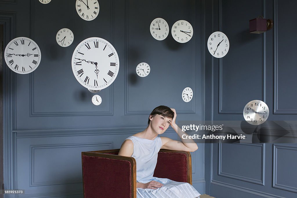 Woman in armchair with hanging clocks above