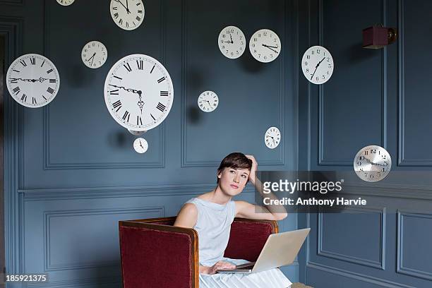 woman using laptop with hanging clocks above - tijdslimiet stockfoto's en -beelden