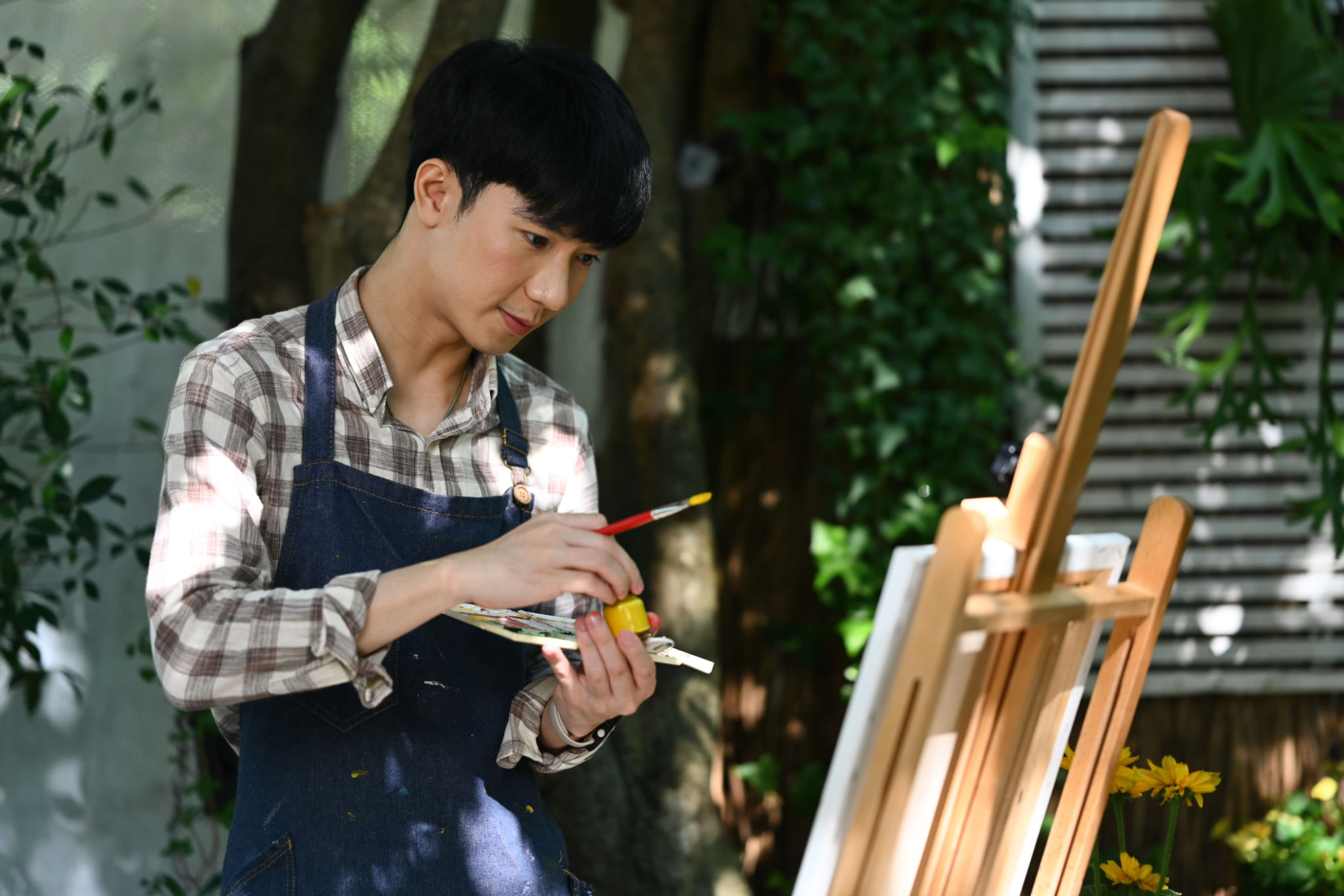 Handsome Asian man in apron painting with watercolor in garden on beautiful day. Handsome Asian man in apron painting with watercolor in garden on beautiful day.