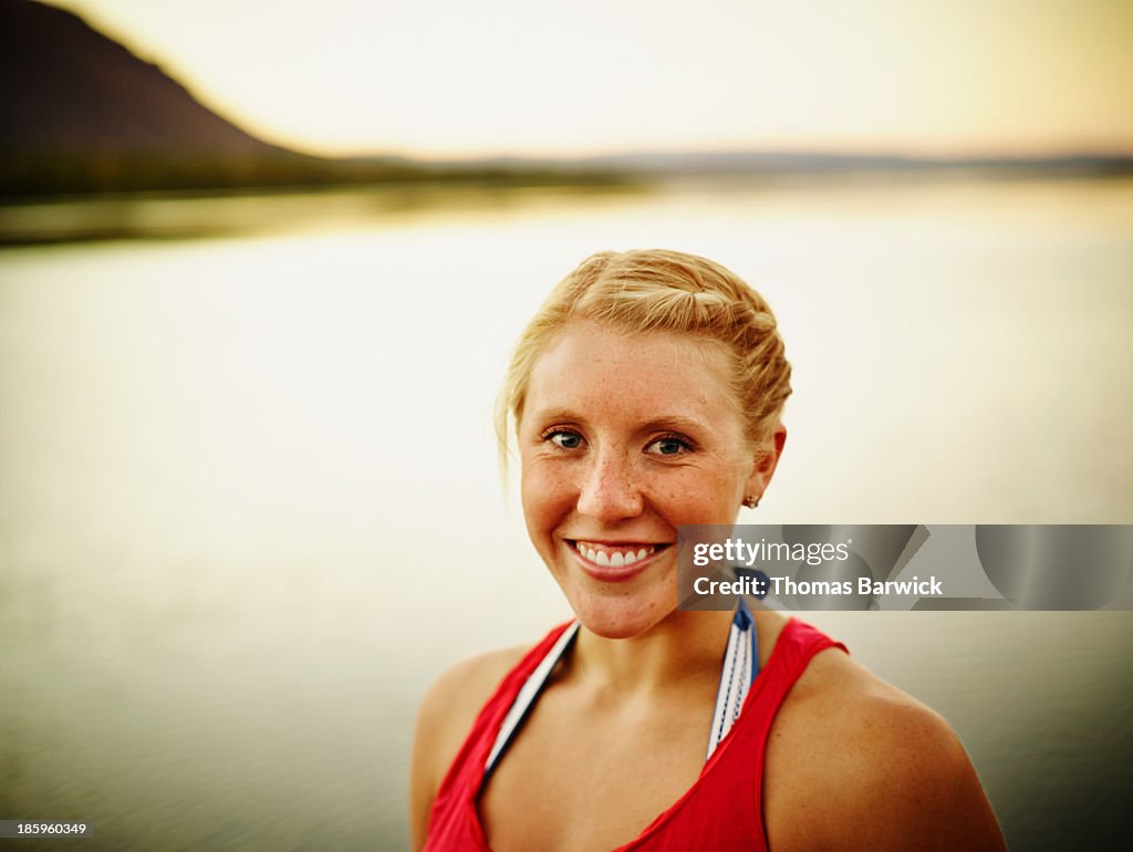 Smiling young woman standing by river at sunset