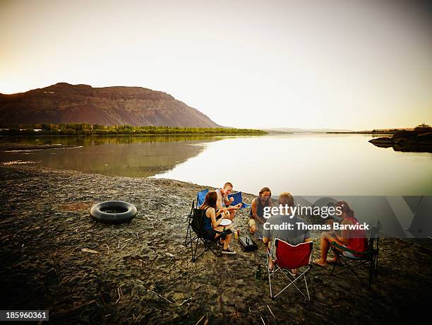 friends eating in camp chairs near river at sunset - 19 to 22 years old stock pictures, royalty-free photos & images